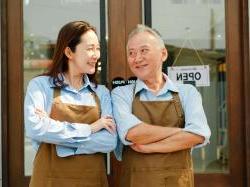 Male and female business owners smiling and standing outside their storefront.